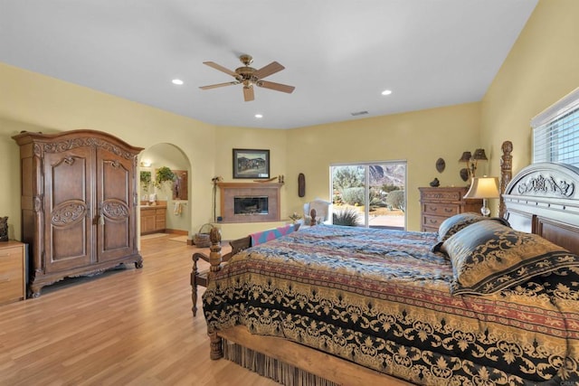 bedroom featuring multiple windows, ceiling fan, light hardwood / wood-style flooring, and a tiled fireplace