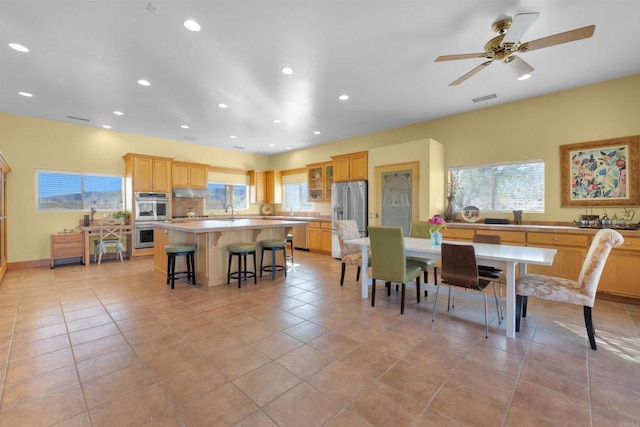 kitchen featuring ceiling fan, stainless steel appliances, a kitchen island, a kitchen breakfast bar, and light tile patterned flooring