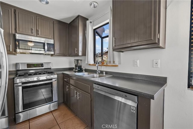 kitchen with appliances with stainless steel finishes, dark brown cabinetry, light tile patterned floors, and sink