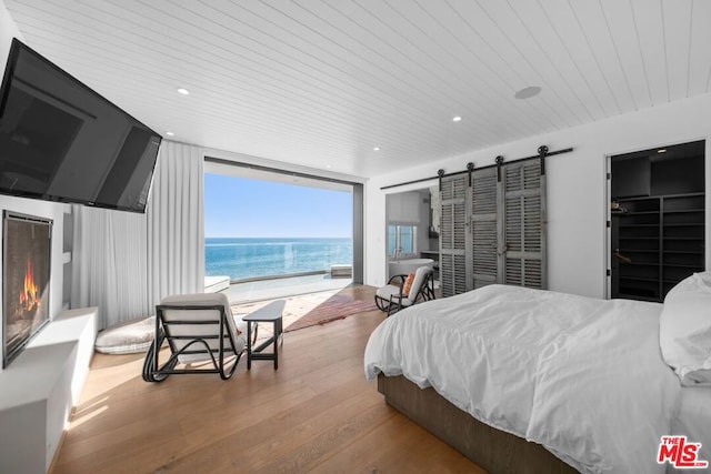 bedroom featuring a spacious closet, a barn door, wood-type flooring, and wooden ceiling