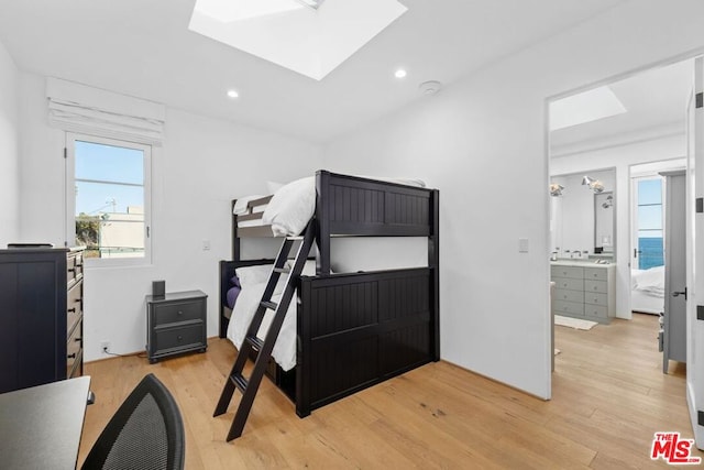 bedroom featuring a water view, light hardwood / wood-style flooring, a skylight, and ensuite bathroom