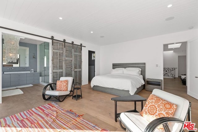 bedroom with connected bathroom, a barn door, and light wood-type flooring