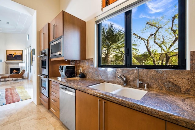 kitchen with sink, stainless steel appliances, tasteful backsplash, dark stone counters, and light tile patterned floors