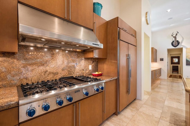 kitchen with light stone countertops, backsplash, paneled fridge, stainless steel gas stovetop, and light tile patterned flooring