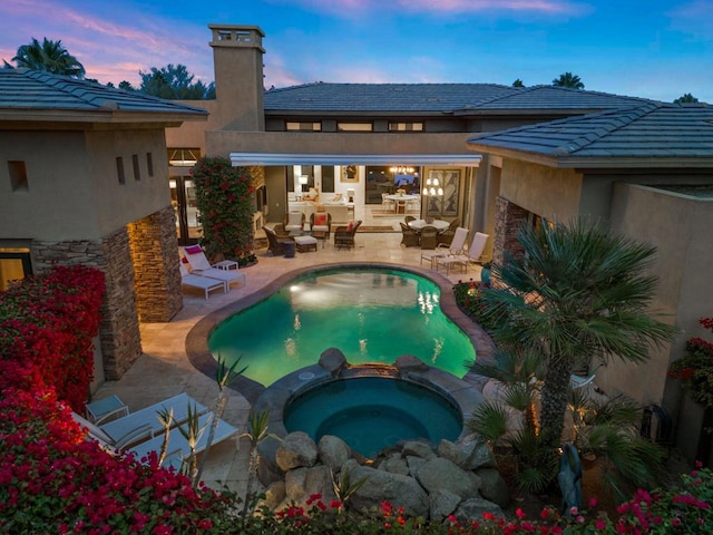 pool at dusk with an in ground hot tub and a patio