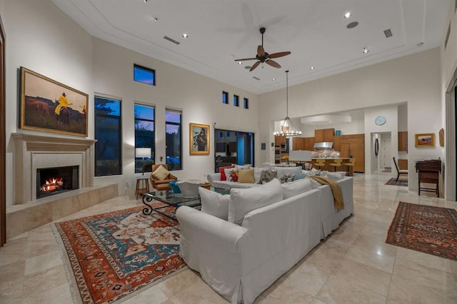 tiled living room with a high ceiling, ceiling fan with notable chandelier, ornamental molding, and a premium fireplace