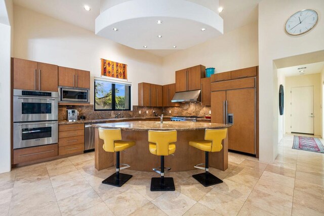 kitchen with built in appliances, a kitchen island with sink, a high ceiling, and a breakfast bar area