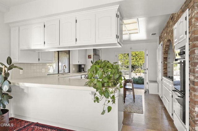 kitchen with kitchen peninsula, backsplash, double oven, sink, and white cabinets