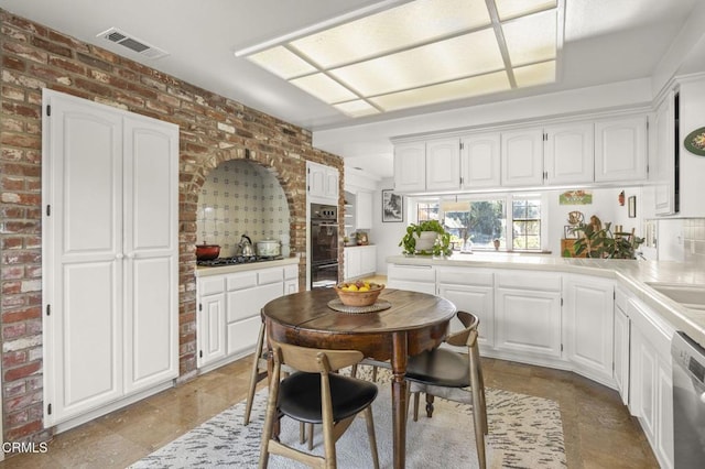 kitchen featuring white cabinets, double oven, dishwasher, and brick wall