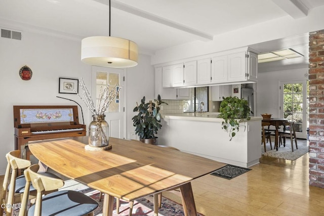 dining room with beamed ceiling, light hardwood / wood-style floors, and sink