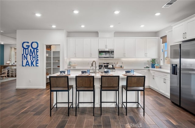 kitchen featuring white cabinetry, dark wood-type flooring, stainless steel appliances, and an island with sink