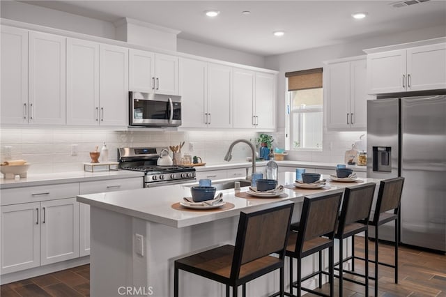 kitchen with dark hardwood / wood-style floors, white cabinetry, a kitchen island with sink, and appliances with stainless steel finishes