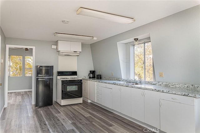 kitchen featuring sink, black fridge, white range with gas stovetop, plenty of natural light, and white cabinets