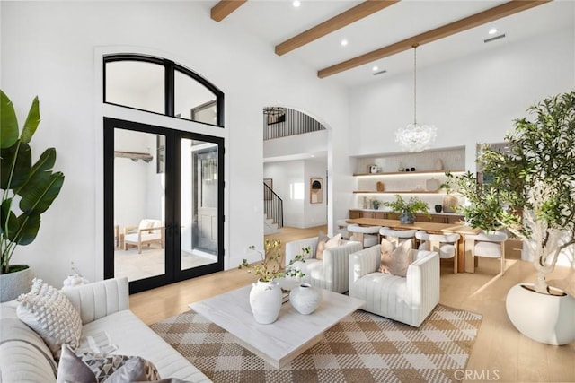 living room with beamed ceiling, light hardwood / wood-style floors, a towering ceiling, and an inviting chandelier