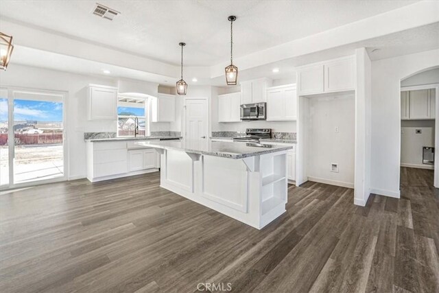 kitchen featuring white cabinetry, a center island, dark stone countertops, appliances with stainless steel finishes, and dark hardwood / wood-style floors