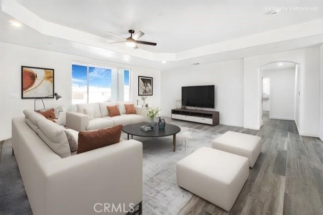 living room featuring wood-type flooring, a raised ceiling, and ceiling fan