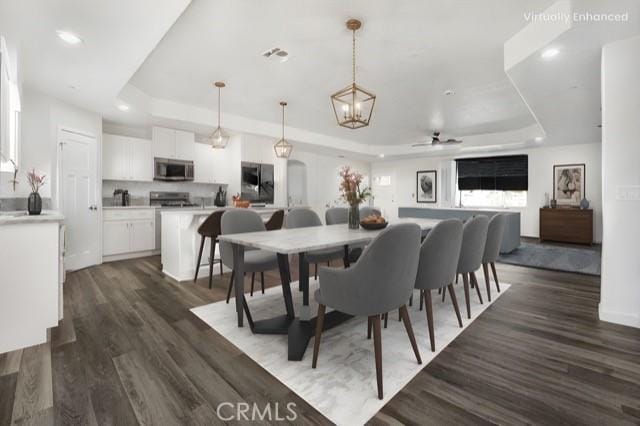 dining room featuring dark wood-type flooring, ceiling fan, and a raised ceiling