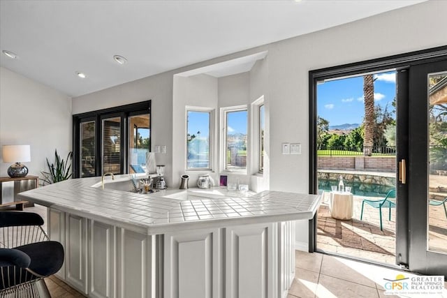 kitchen with tile countertops, plenty of natural light, light tile patterned flooring, and white cabinets