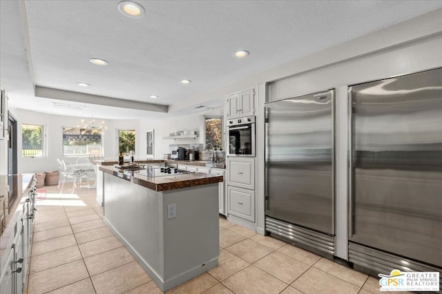 kitchen with appliances with stainless steel finishes, light tile patterned floors, white cabinets, a center island, and a chandelier