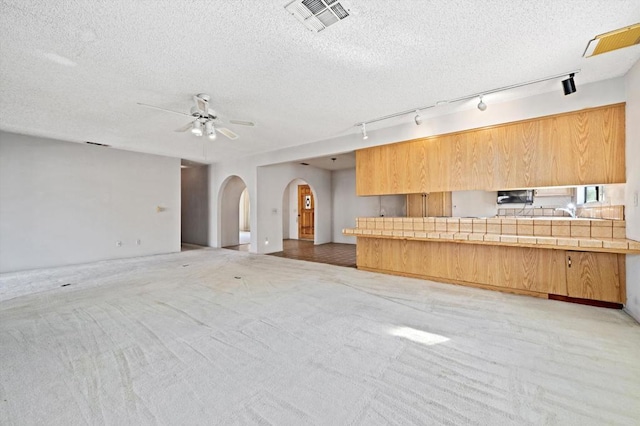 kitchen featuring a textured ceiling, light colored carpet, track lighting, and tile counters