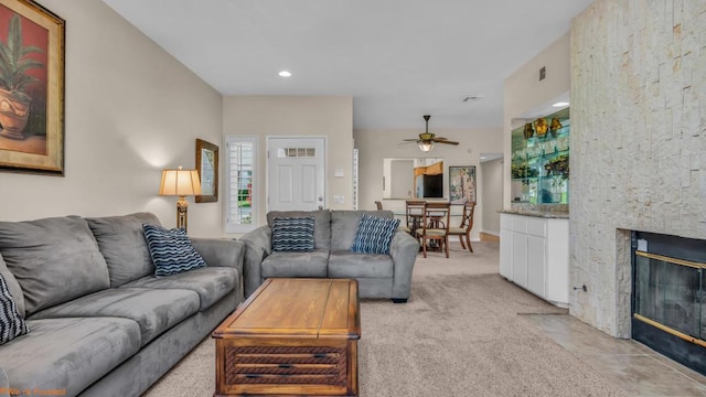 living room featuring ceiling fan, a fireplace, and light colored carpet