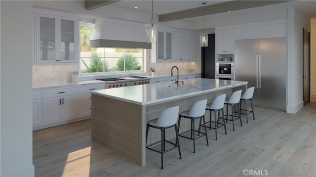 kitchen featuring white cabinetry, stainless steel appliances, an island with sink, a kitchen bar, and wall chimney exhaust hood