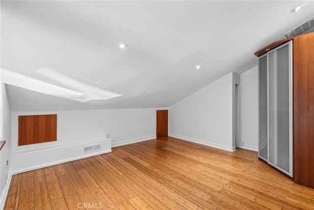 additional living space with a textured ceiling, vaulted ceiling, and light hardwood / wood-style flooring