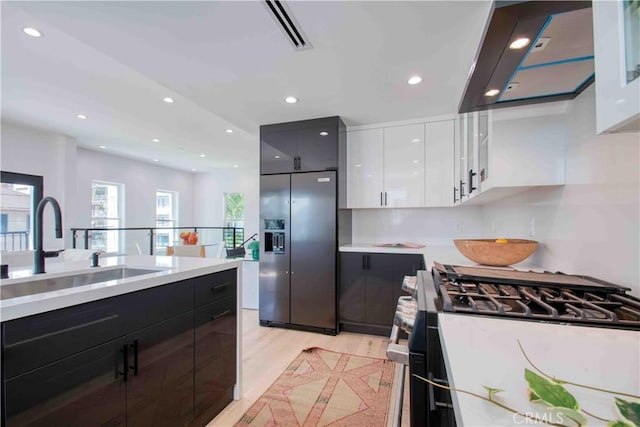 kitchen featuring white cabinetry, sink, stainless steel fridge with ice dispenser, gas range oven, and light hardwood / wood-style floors