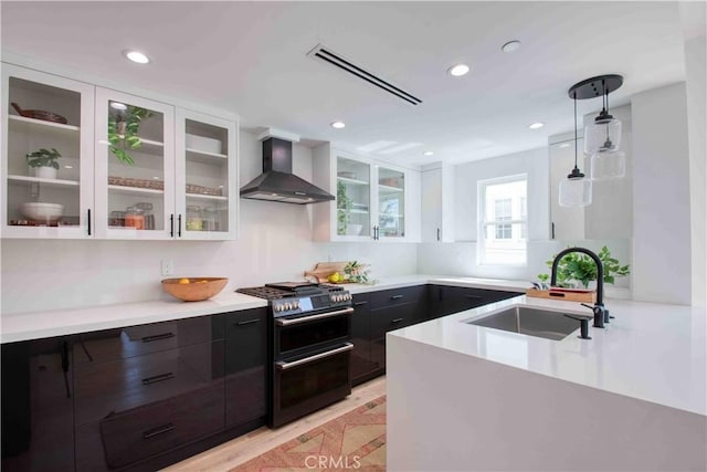 kitchen featuring wall chimney exhaust hood, sink, pendant lighting, white cabinets, and stainless steel range with gas cooktop