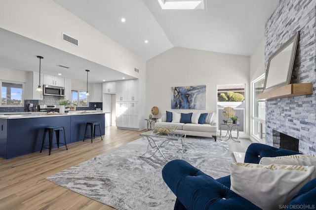 living room with a fireplace, light hardwood / wood-style flooring, high vaulted ceiling, and plenty of natural light