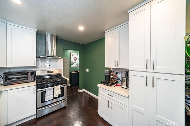 kitchen with white cabinets, wall chimney range hood, stainless steel gas range, dark hardwood / wood-style floors, and tasteful backsplash