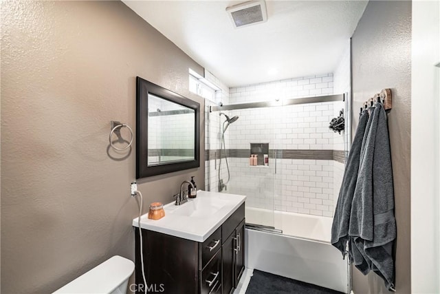 bathroom featuring shower / bath combination with glass door, visible vents, a textured wall, toilet, and vanity