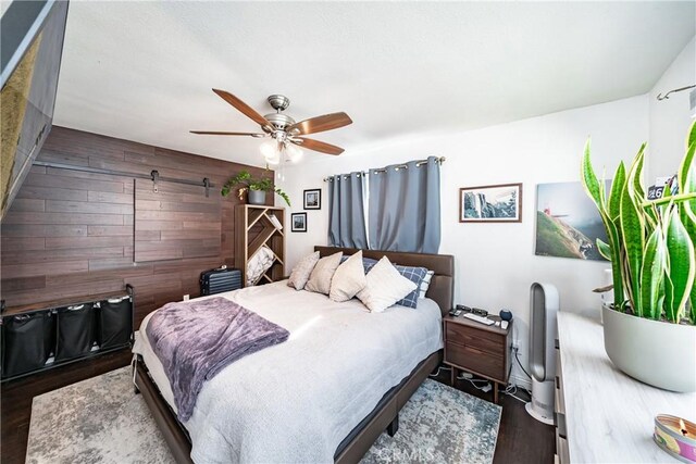 bedroom featuring ceiling fan, wood walls, and dark wood-type flooring