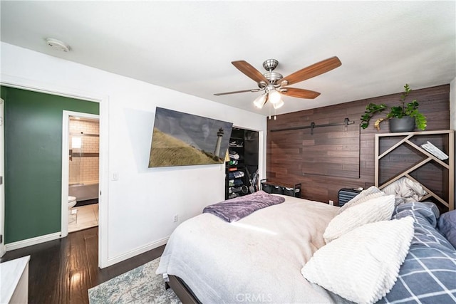 bedroom featuring ceiling fan, dark hardwood / wood-style floors, ensuite bathroom, and wooden walls