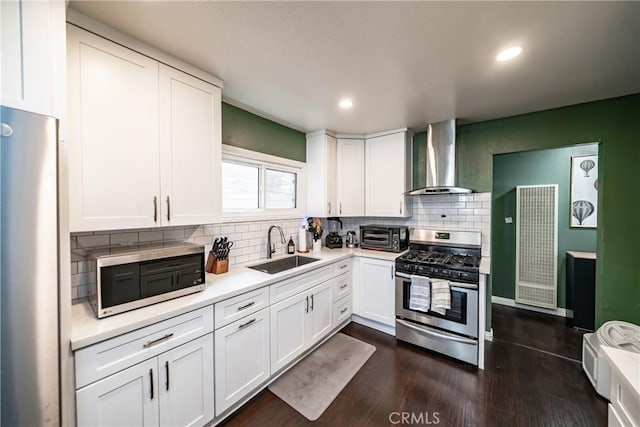 kitchen with a sink, white cabinets, light countertops, wall chimney range hood, and appliances with stainless steel finishes