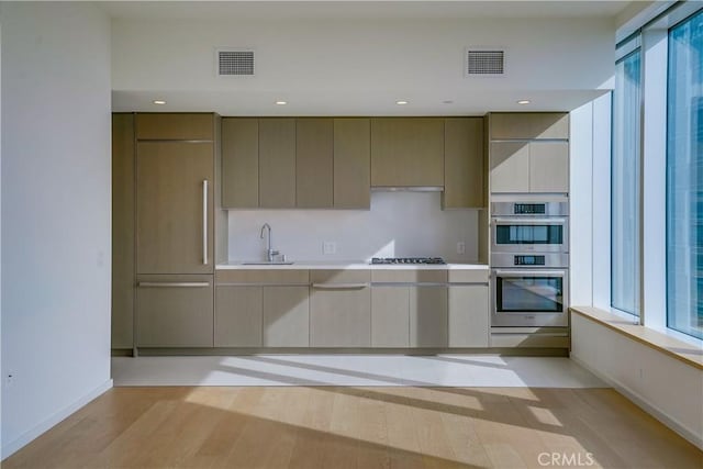 kitchen with double oven, sink, gas cooktop, and light wood-type flooring