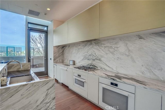 kitchen with decorative backsplash, light wood-type flooring, white oven, sink, and white cabinetry