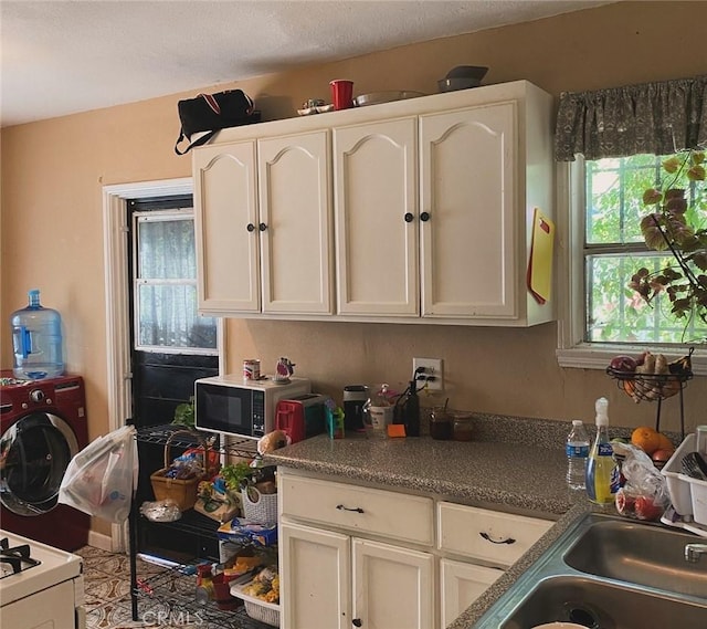 kitchen featuring white range oven, washer / dryer, and white cabinetry