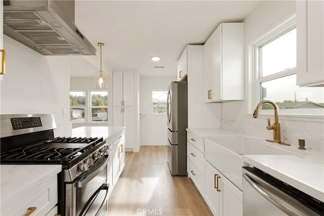 kitchen featuring wall chimney range hood, appliances with stainless steel finishes, decorative light fixtures, light stone counters, and white cabinetry