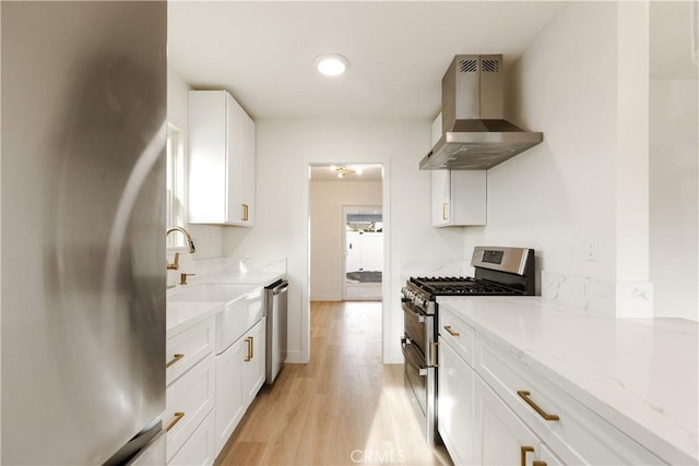 kitchen featuring wall chimney exhaust hood, stainless steel appliances, sink, light hardwood / wood-style flooring, and white cabinets