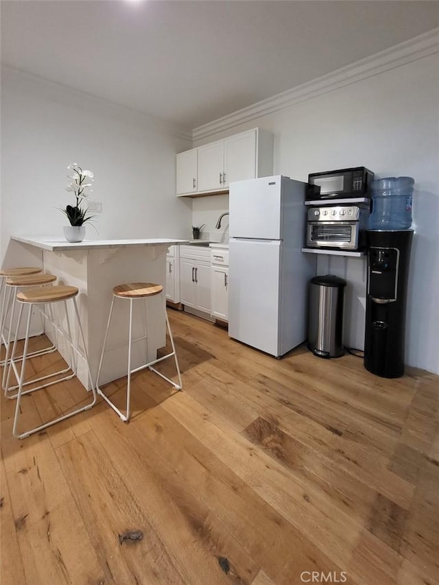 kitchen with white fridge, a breakfast bar area, light wood-type flooring, ornamental molding, and white cabinetry