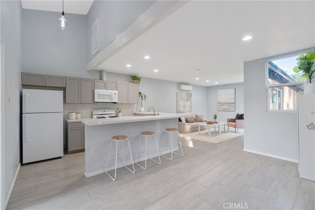 kitchen featuring white appliances, a kitchen island with sink, gray cabinetry, hanging light fixtures, and a kitchen bar