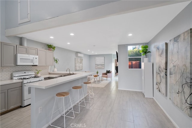 kitchen with white appliances, a kitchen breakfast bar, backsplash, gray cabinets, and a kitchen island with sink