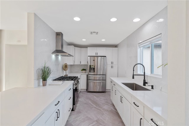 kitchen featuring appliances with stainless steel finishes, light countertops, a sink, and wall chimney range hood