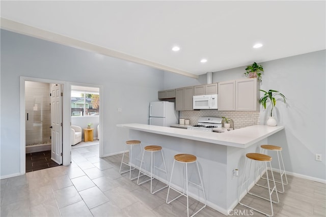 kitchen with white appliances, kitchen peninsula, a breakfast bar, sink, and tasteful backsplash