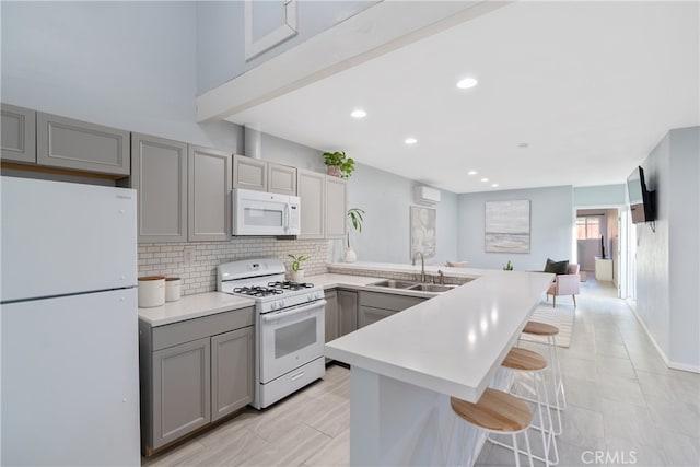 kitchen with sink, a breakfast bar area, white appliances, and gray cabinetry