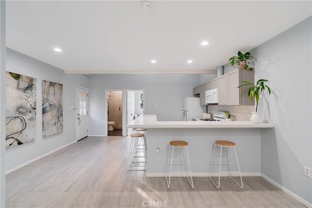 kitchen featuring white appliances, white cabinets, kitchen peninsula, and a kitchen bar