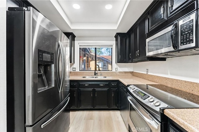 kitchen featuring a tray ceiling, sink, light hardwood / wood-style floors, and appliances with stainless steel finishes