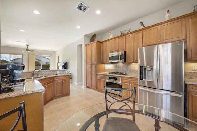 kitchen featuring light stone countertops, tasteful backsplash, stainless steel appliances, ceiling fan, and sink