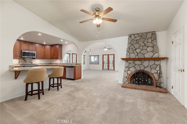 kitchen with kitchen peninsula, a kitchen breakfast bar, light carpet, stainless steel appliances, and a stone fireplace